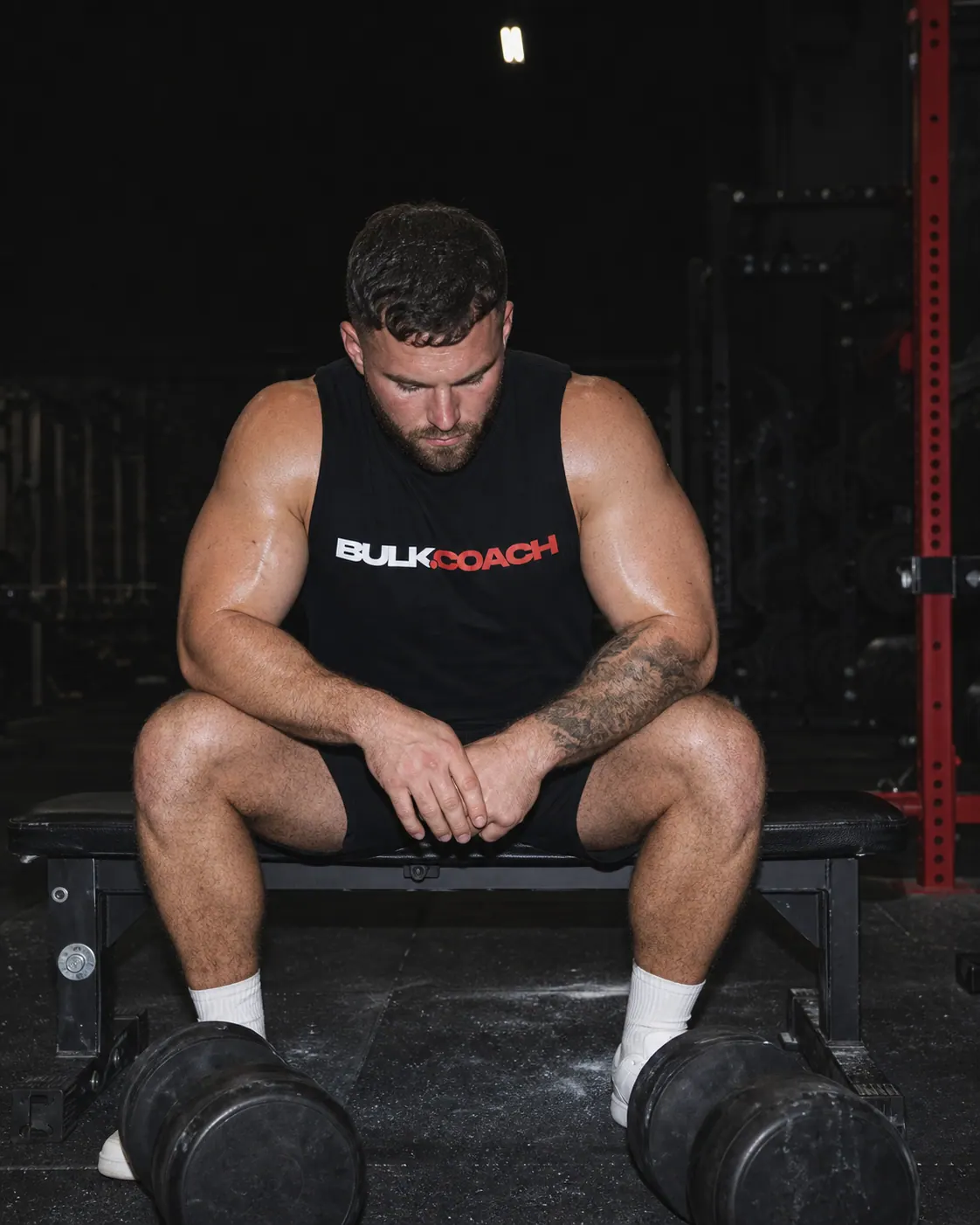 An adult lifter resting between dumbbell sets in a dark independent gym